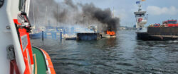 Das Seenotrettungsboot ERICH KOSCHUBS nähert sich dem brennenden Havaristen. Die Priwallfähre „Pötenitz“ bringt Feuerwehrleute von der Wasserseite aus zum Unglücksort.