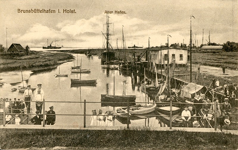 Kleine Segelboote liegen im Alten Hafen von Brunsbüttel, an Land stehen Segelnde in Matrosenkleidung. Das historische Foto zeigt das Geschehen um 1930.