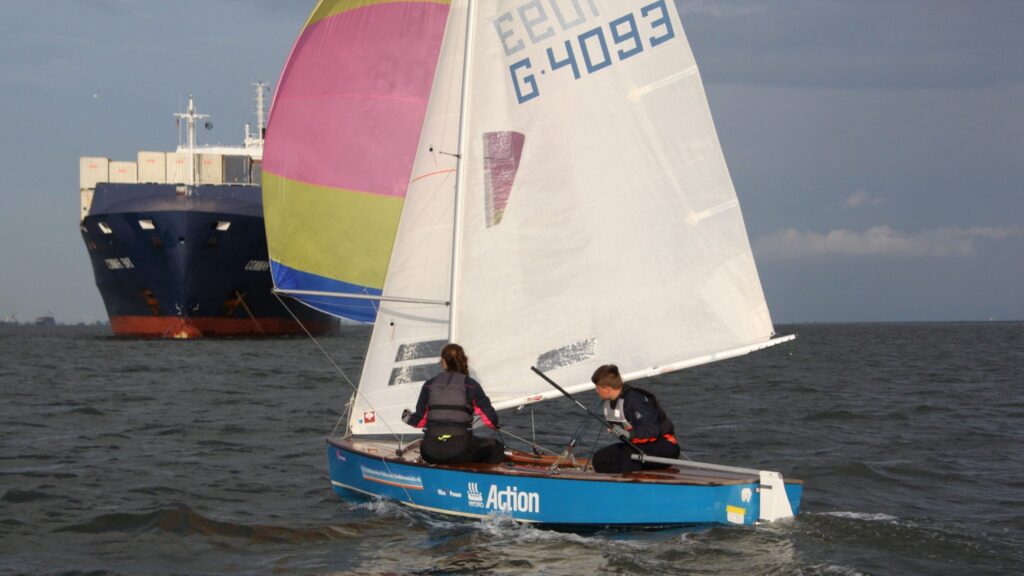 Ein Pirat mit zwei Segelnden an Bord ist auf der Elbe unterwegs und muss den großen Frachtern auf dem Fluss ausweichen.