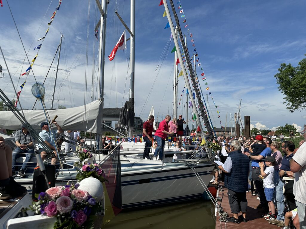 Geschmückte Yachten liegen am Steg. Auf dem Steg feiern viele Menschen die neuen Boote und neuen Vereinsmitglieder.