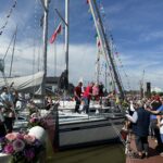 Geschmückte Yachten liegen am Steg. Auf dem Steg feiern viele Menschen die neuen Boote und neuen Vereinsmitglieder.