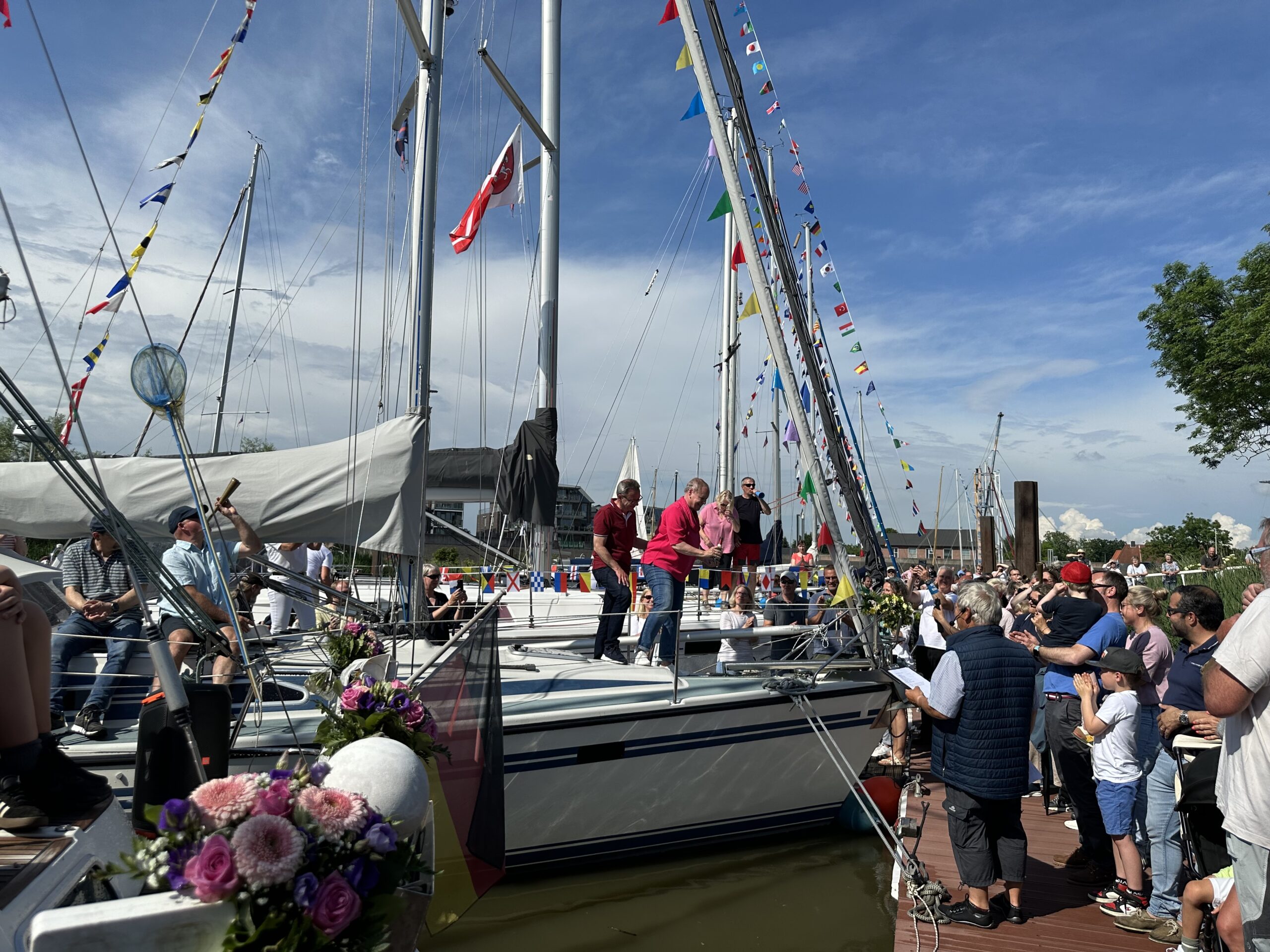 Geschmückte Yachten liegen am Steg. Auf dem Steg feiern viele Menschen die neuen Boote und neuen Vereinsmitglieder.