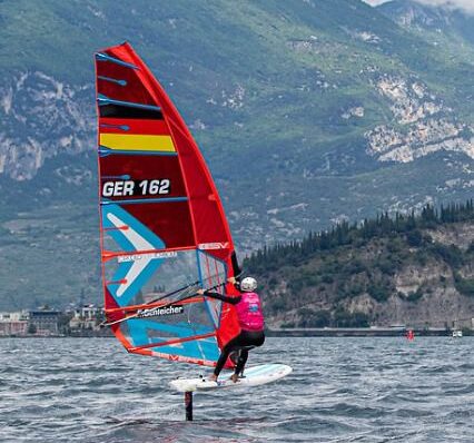 Die Windsurferin Emma Schleicher foilt mit ihrem iQFOiL-Board über den Gardasee. Im Hintergrund sind Berge zu sehen.