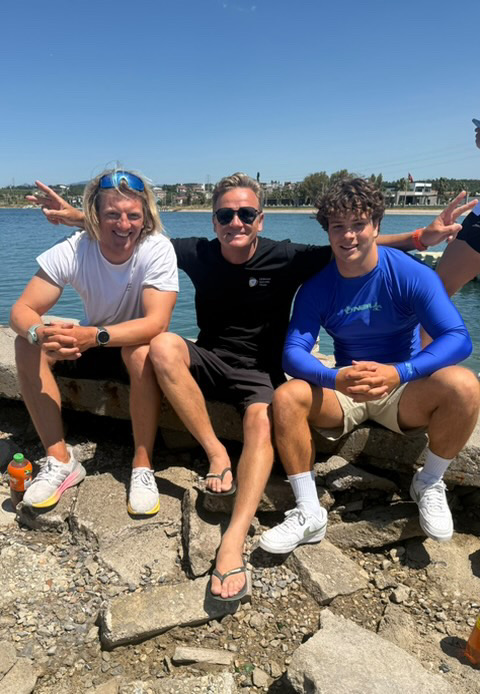Jannis Maus, DSV-Trainer Aleksei Chibizov und Jan Vöster sitzen auf einer Mauer. Sie lächeln in die Kamera. Im Hintergrund ist das Meer zu sehen