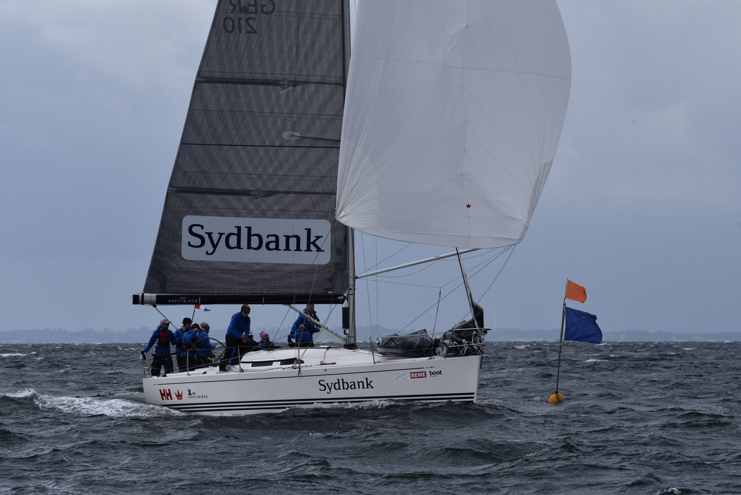Eine Regattayacht bei viel Wind vor der blauen Zieltonne.