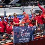 Eine Crew mit roten T-Shirts feiert auf einer roten Yacht einen Regattaerfolg