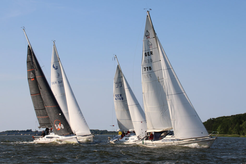 Vier Segelboote segeln im Strelasund. Sie sind gerade zur Regatta Rund Rügen gestartet. Der Wind bläst stark, einige Boote haben ein Reff im Großsegel