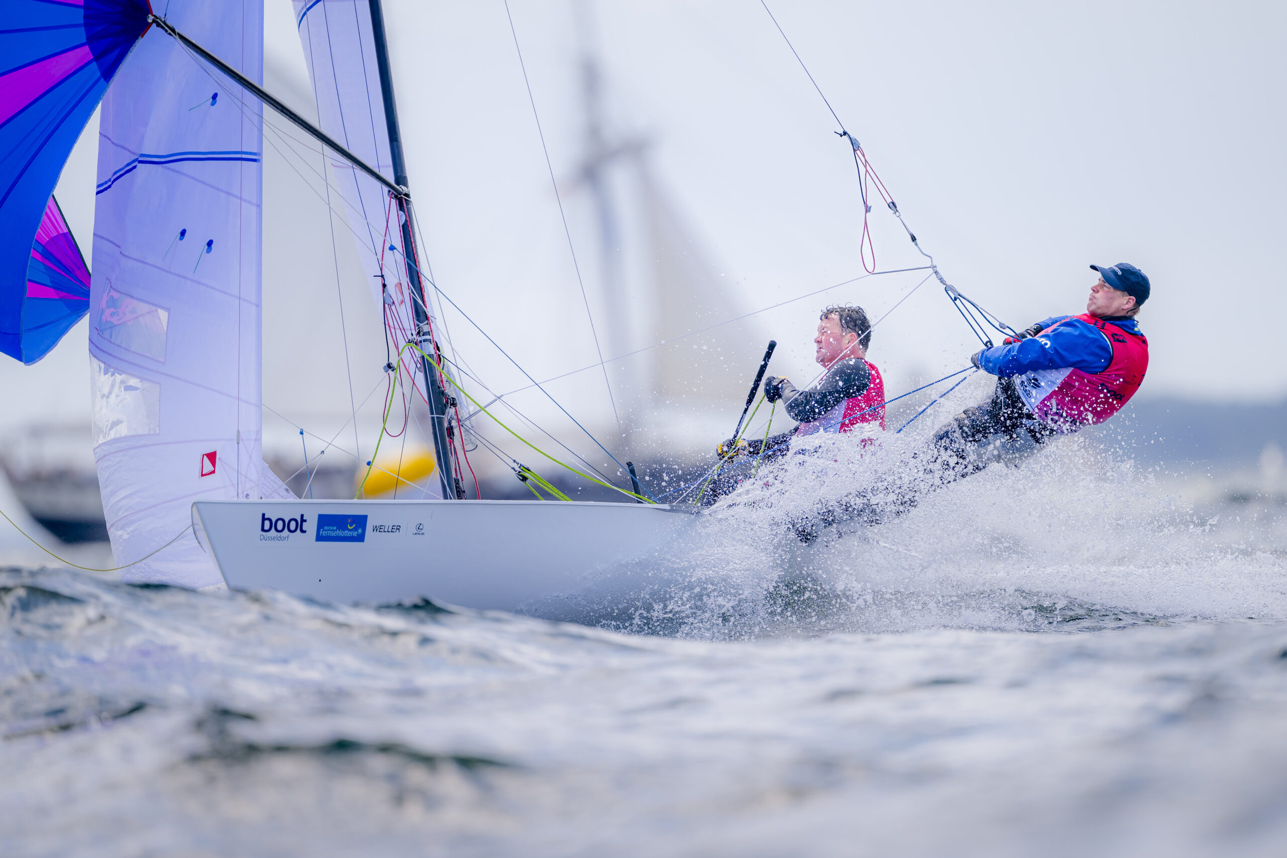 Zwei Männer mit einem pinkfarbenen Trikot segeln auf einer weißen Jolle mit Trapez.