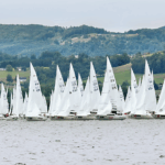 Flotte von H-Booten auf dem Traunsee vor grünen Feldern und Hügeln.