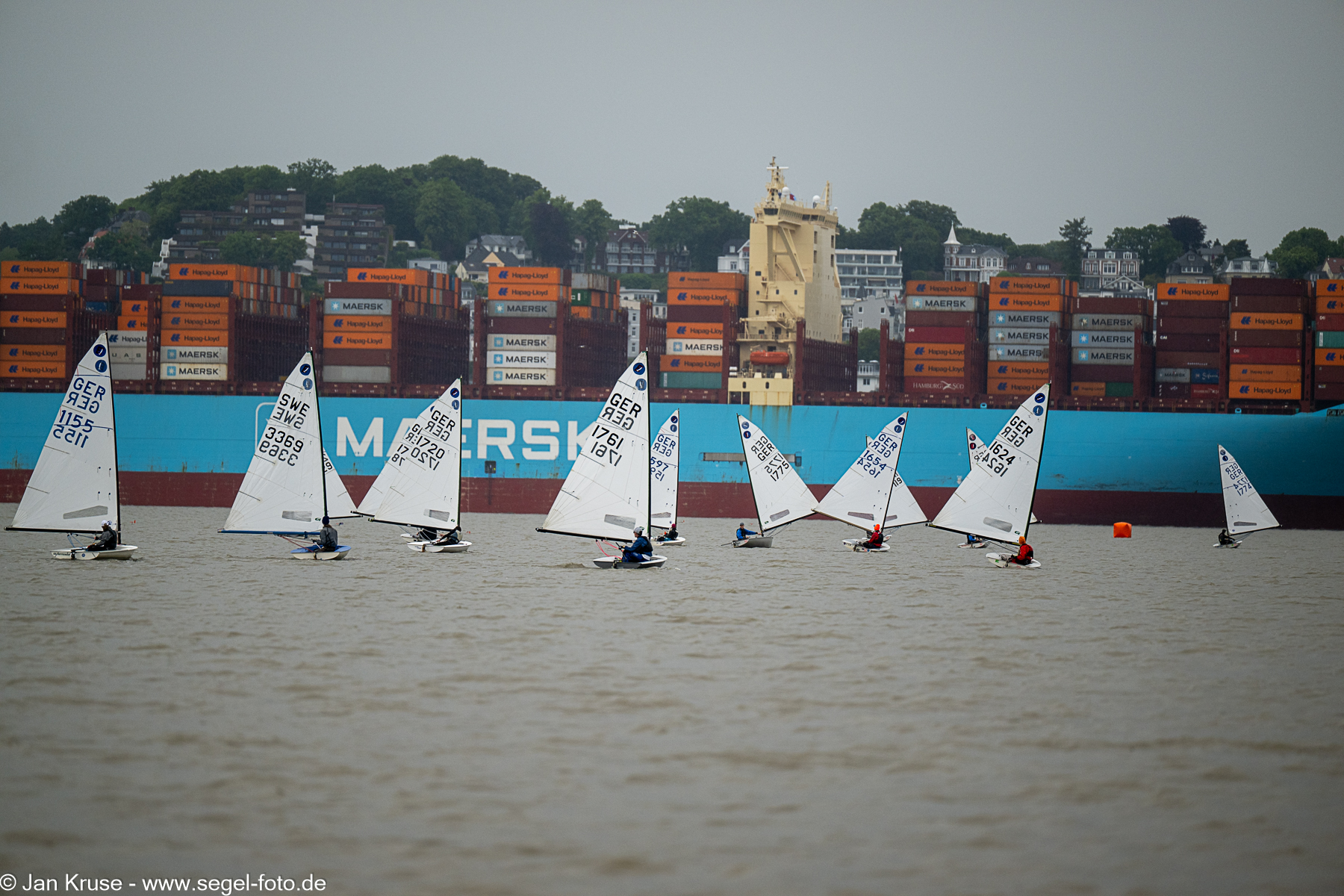Jollen der Europe-Klasse auf der Elbe vor einem beladenen Containerschiff.