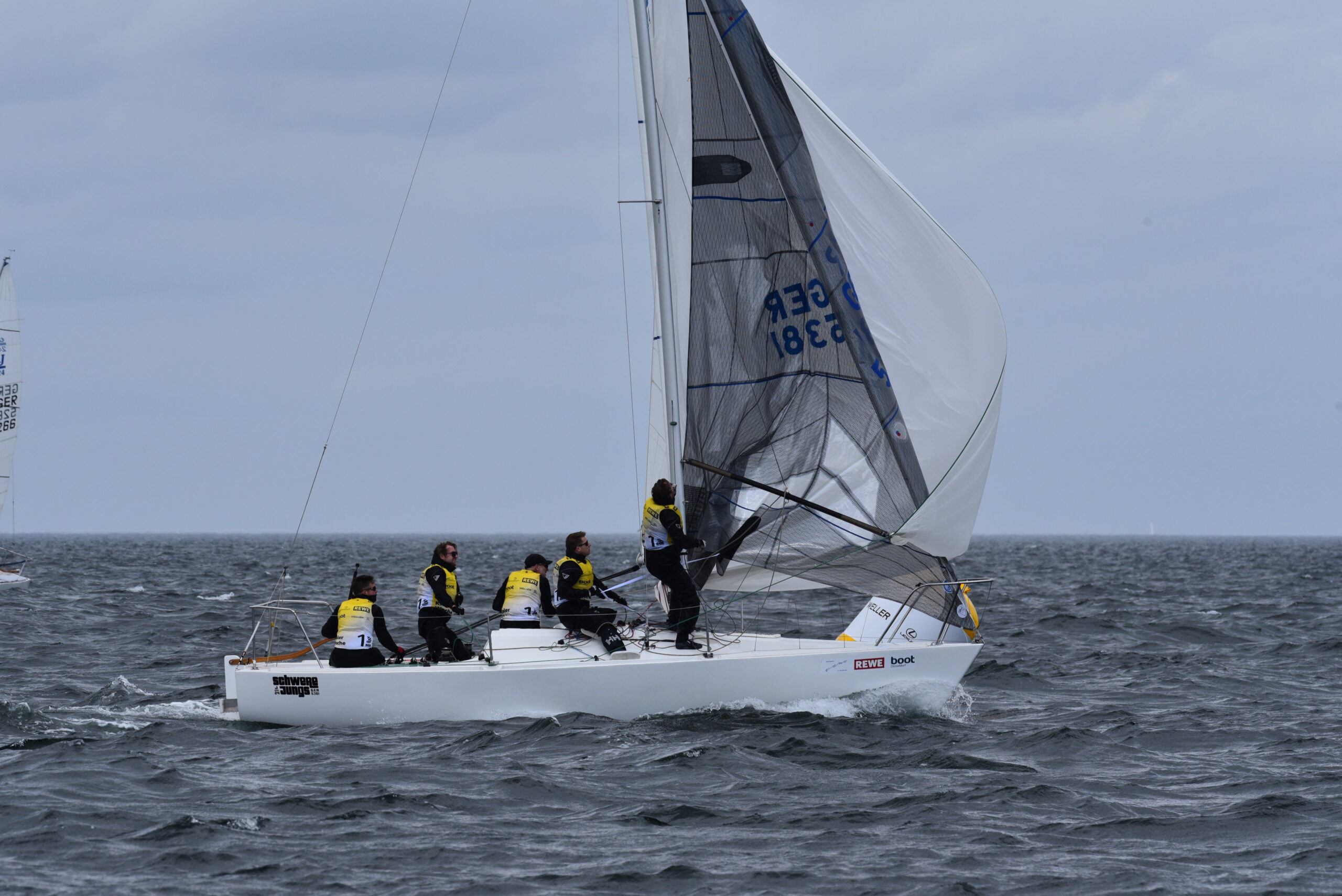 Segler mit gelben Trikots bergen auf einem Kielboot vom Typ J/24 den Spinnaker.