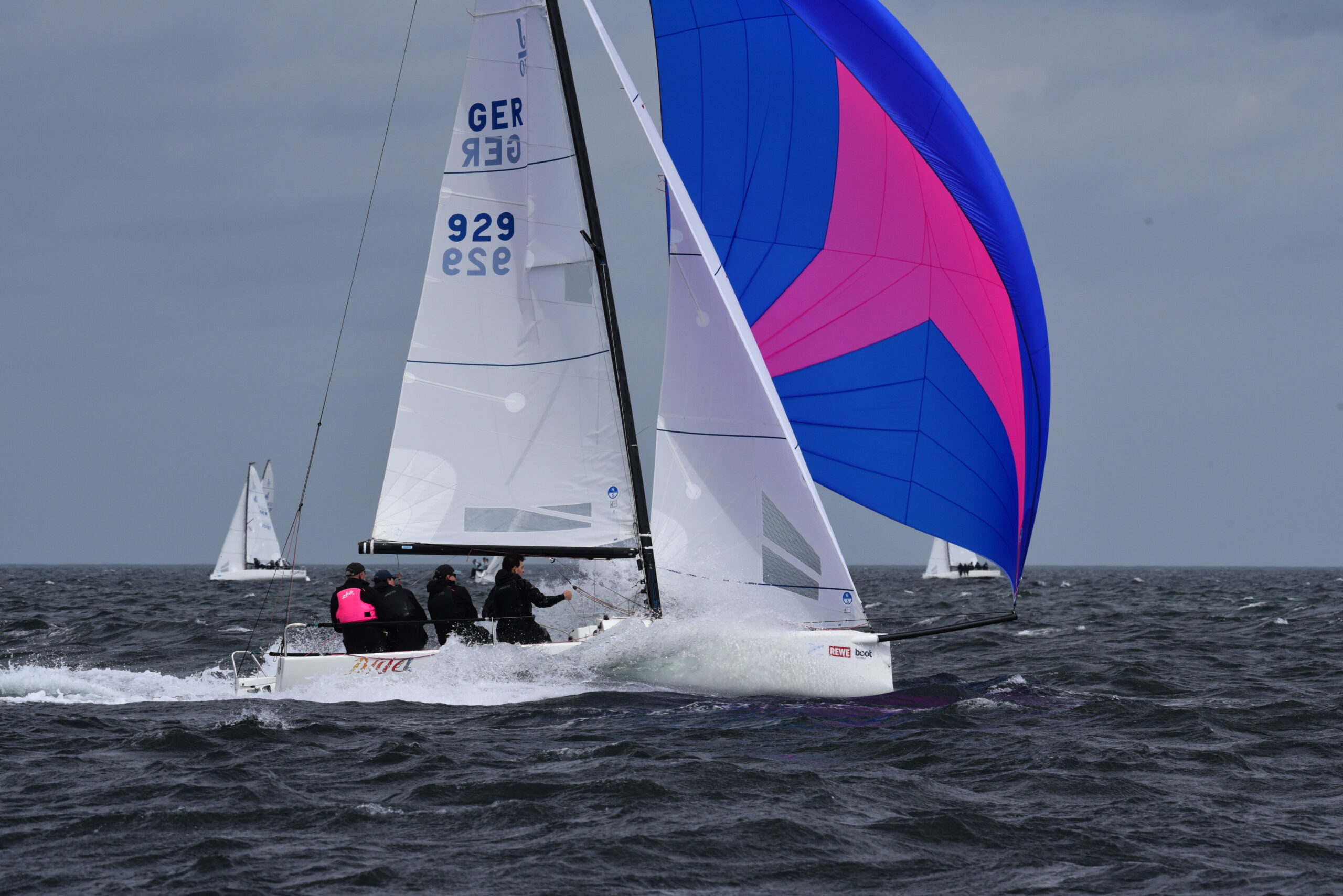 Eine weiße Segelyacht mit einem blau-pinken Spinnaker.