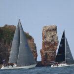 Zwei Yachten mit schwarzen Segeln vor der Langen Anna, dem charakteristischen Felsvorsprung der Nordseeinsel Helgoland.