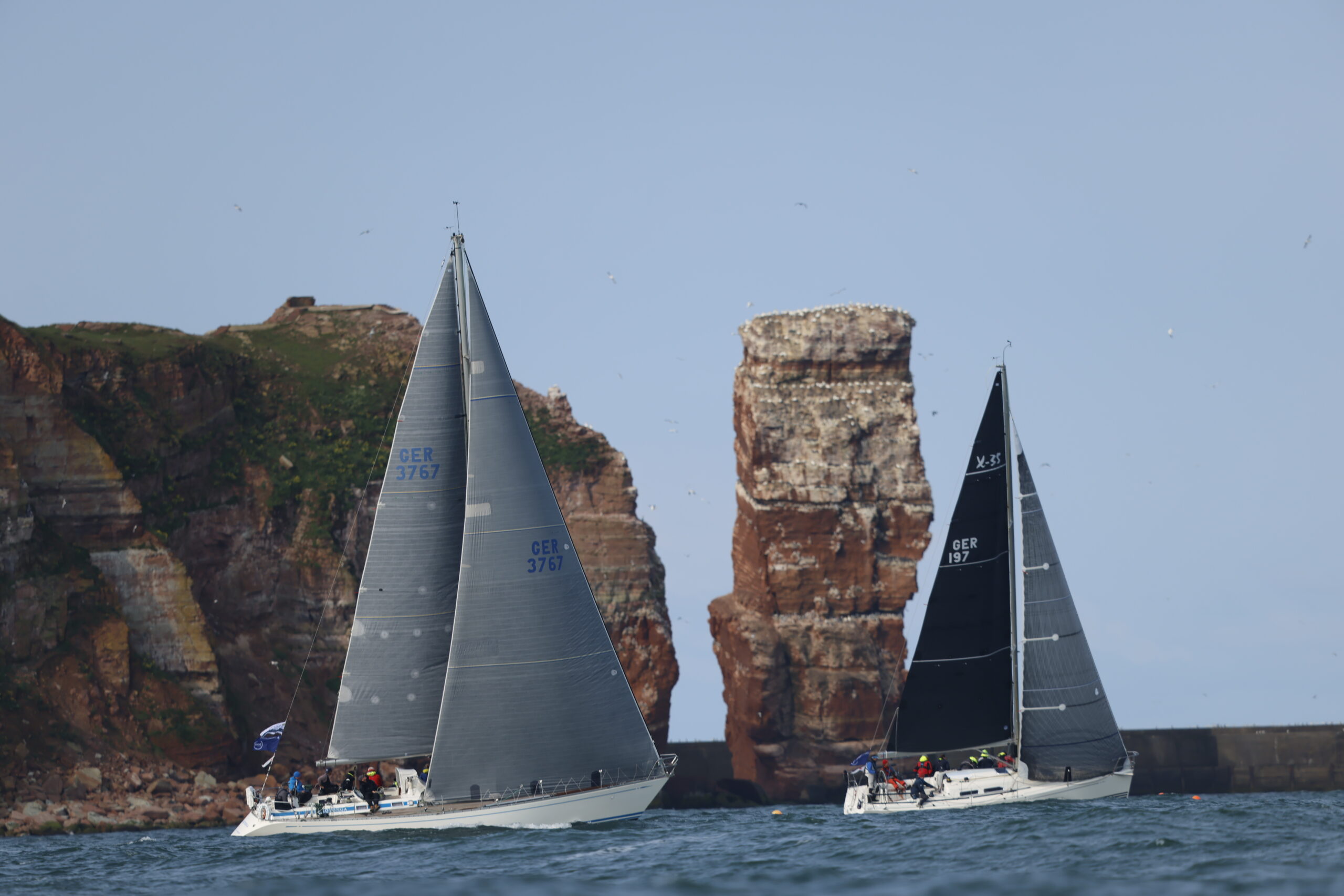 Zwei Yachten mit schwarzen Segeln vor der Langen Anna, dem charakteristischen Felsvorsprung der Nordseeinsel Helgoland.