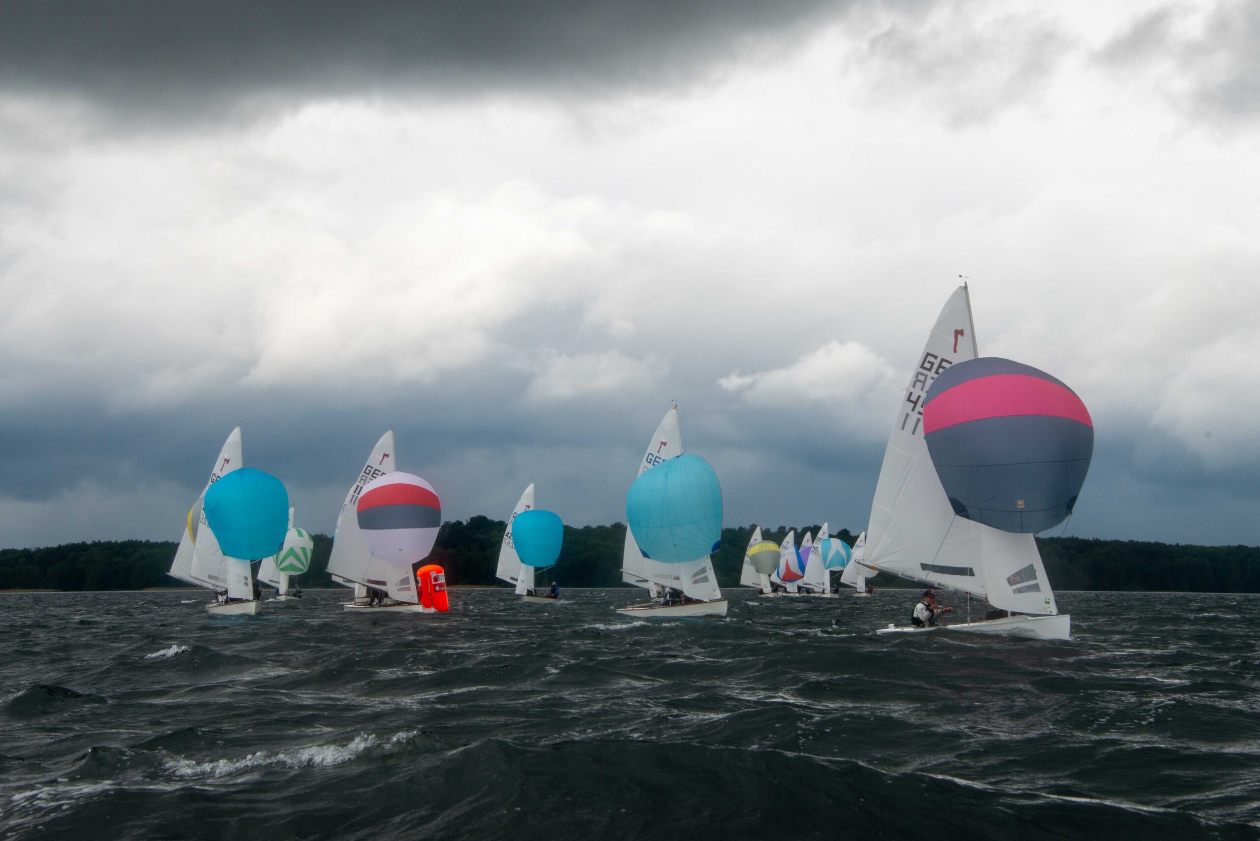 Die bunten Spinnaker der Piraten-Jollen leuchten vor einer dunklen Regenwolke.