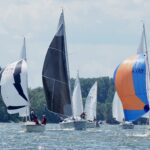 Bei glitzerndem Sonnenlicht segeln Boote eine Wettfahrt auf dem Rhein. Einige haben große bunte Segel, so genannte Spinnaker, hochgezogen.