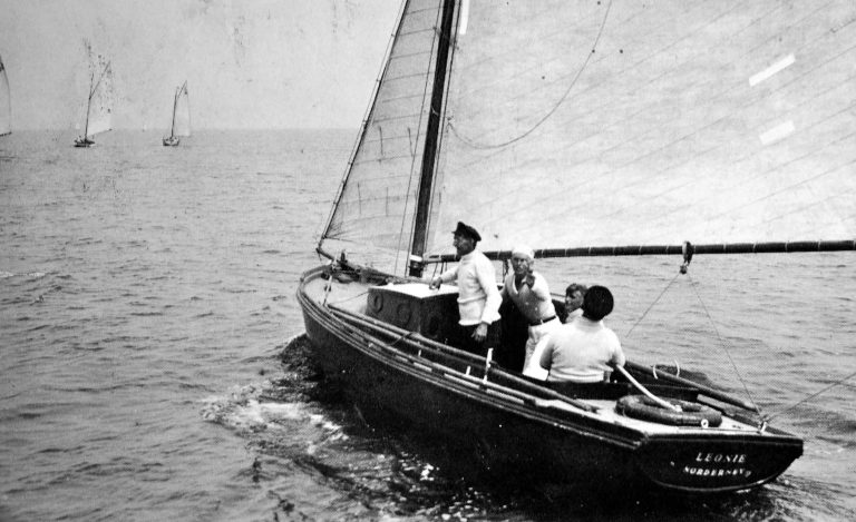 Das Schwarz-Weiß-Foto zeigt vier Männer im Cockpit eines Segelboots, die Segel sind hochgezogen. Es ist altes Foto aus den Jahren um 1930