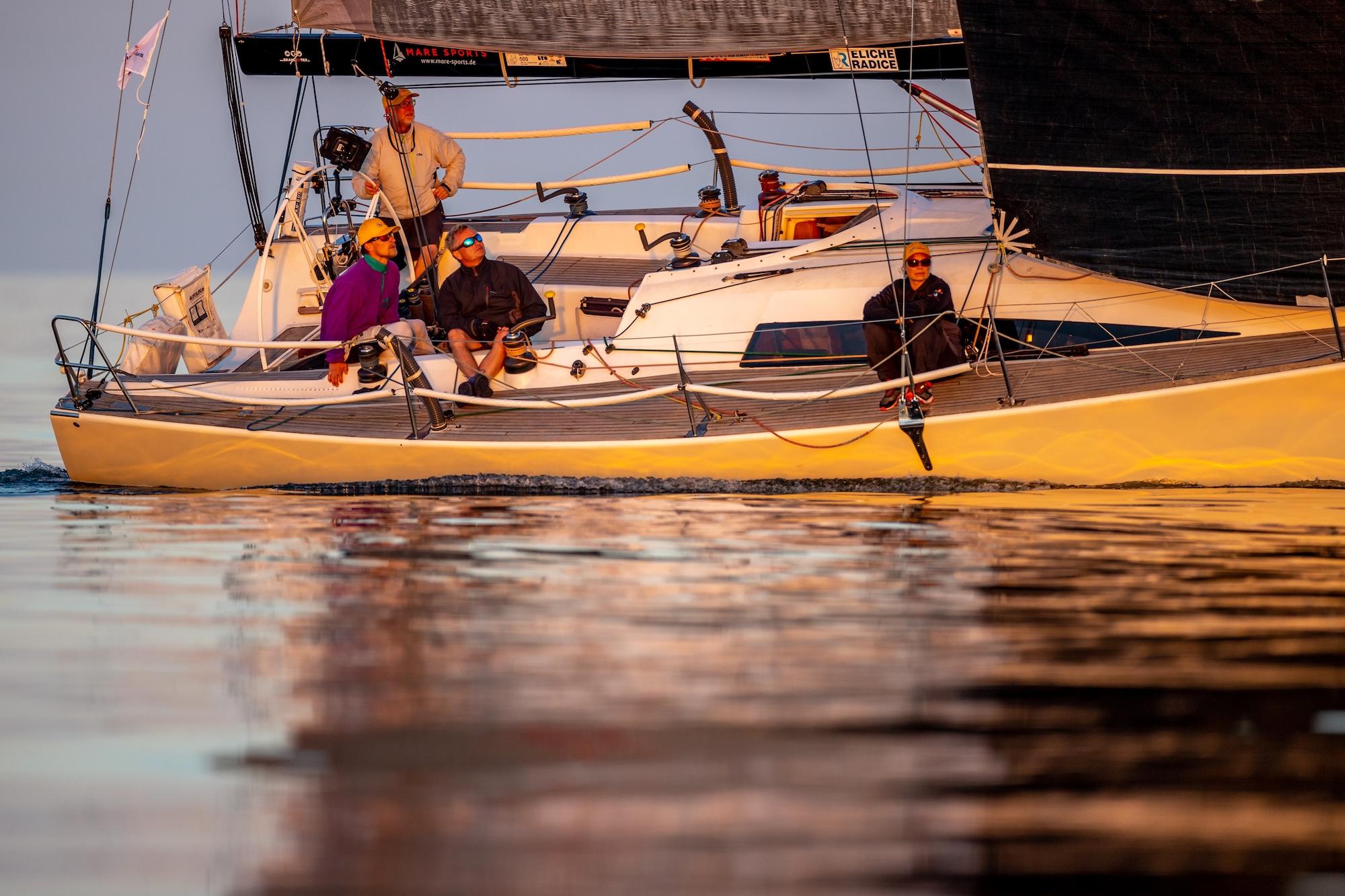 Eine Yacht mit einem gelben Rumpf bei wenig Wind und glänzendem Wasser.