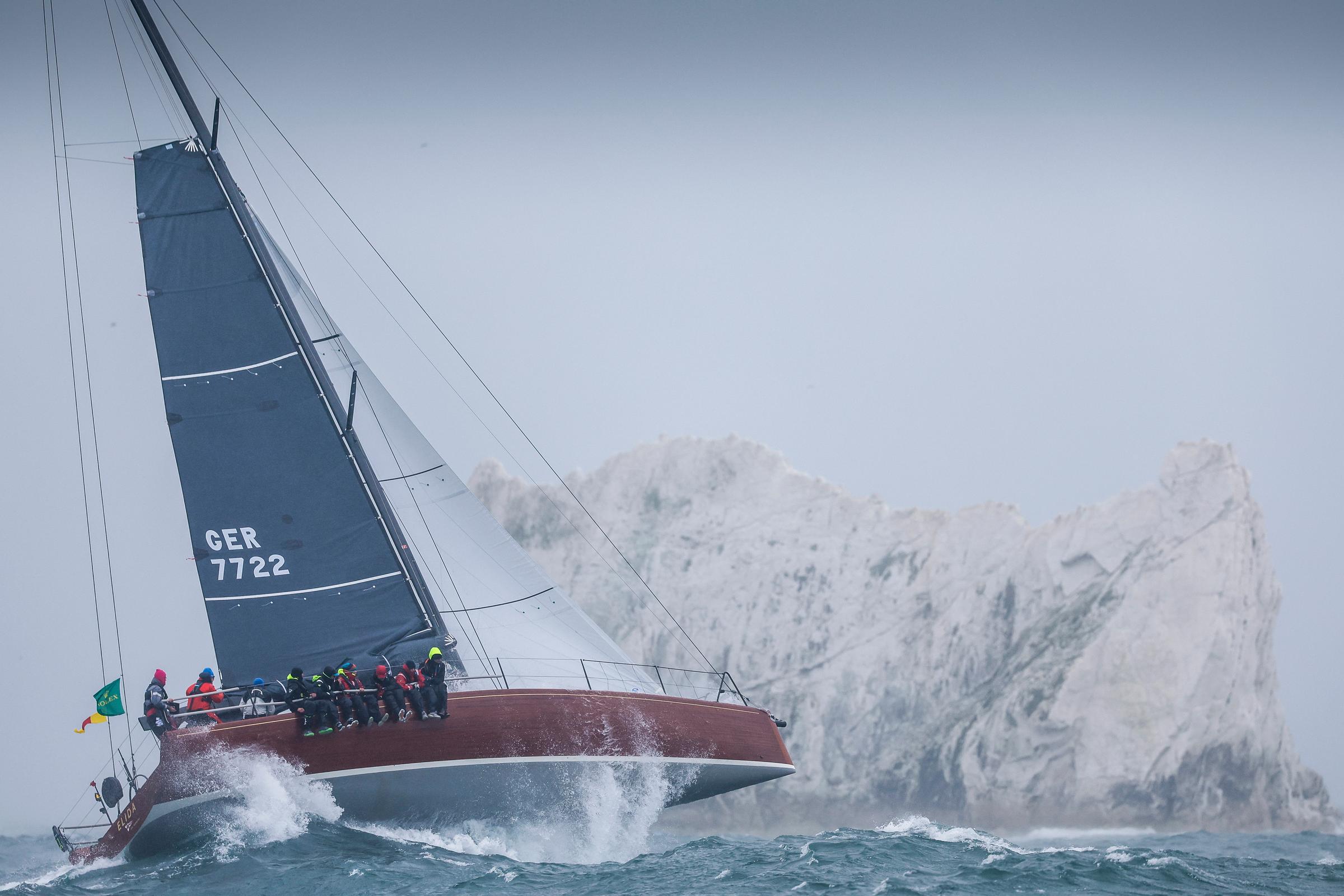 Eine Yacht mit einem Holzrumpf vor einem hellen, zackigen Felsen.