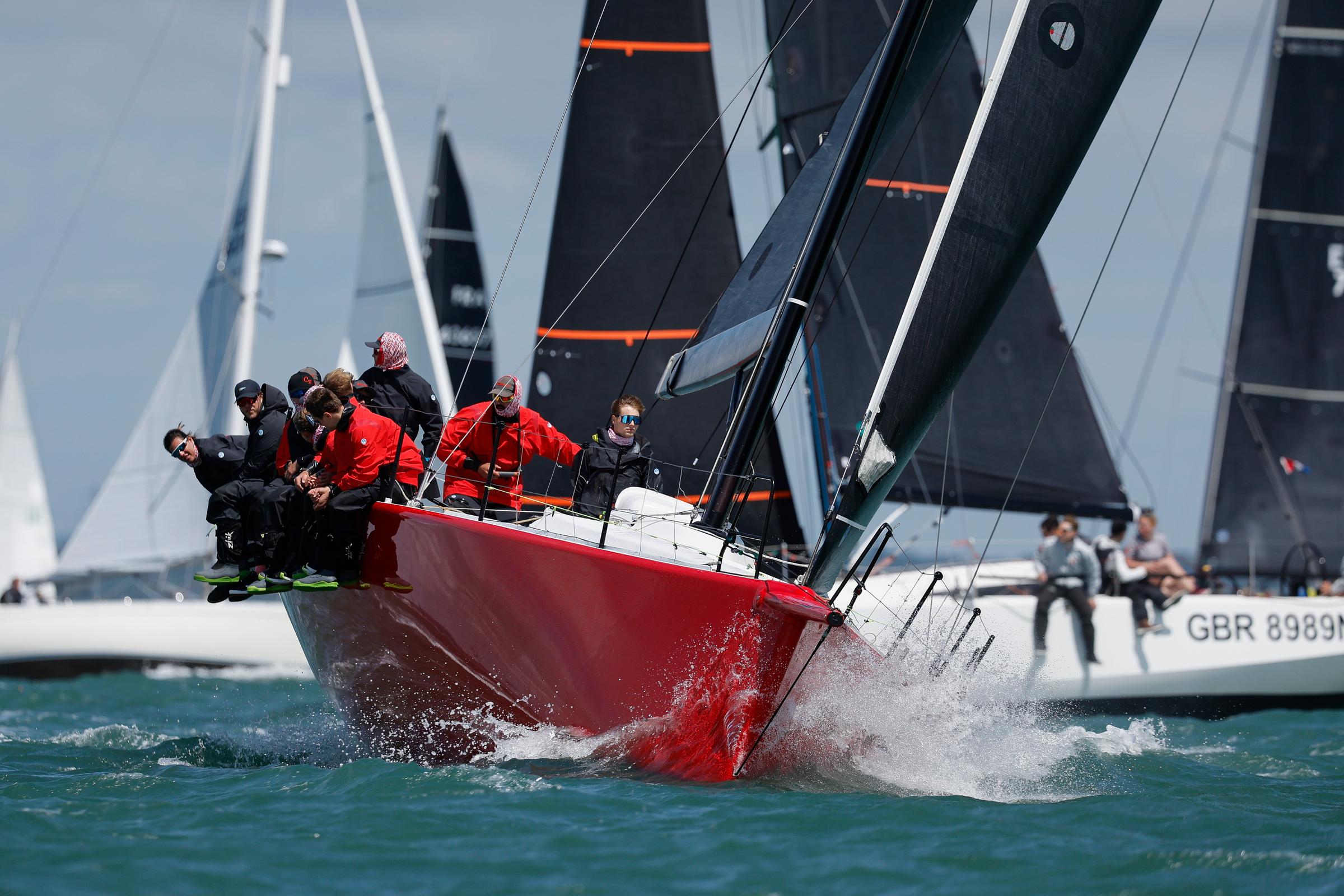 Eine rote Yacht, die Segler sitzen in rotem und schwarzem Ölzeug auf der sogenannten hohen Kante.