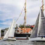 Drei Yachten mit weißen Segeln vor der Viermastbark Passat in Travemünde.