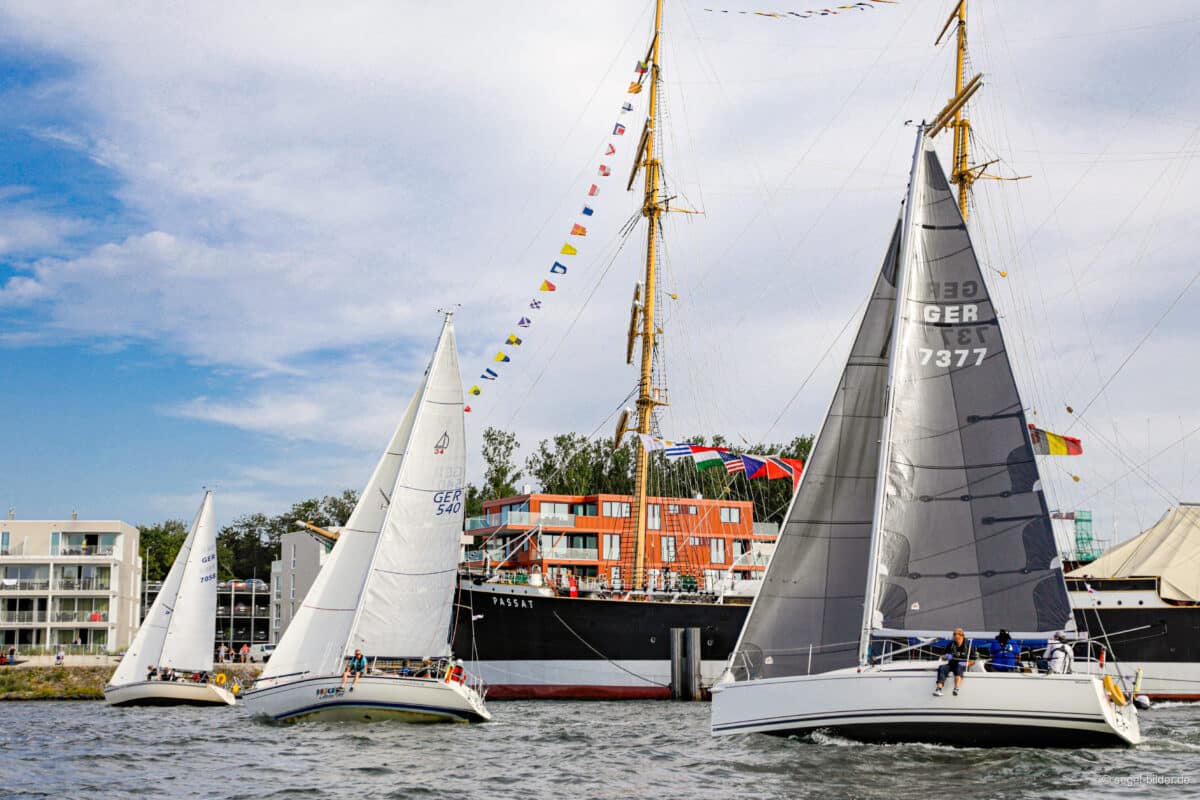 Drei Yachten mit weißen Segeln vor der Viermastbark Passat in Travemünde.