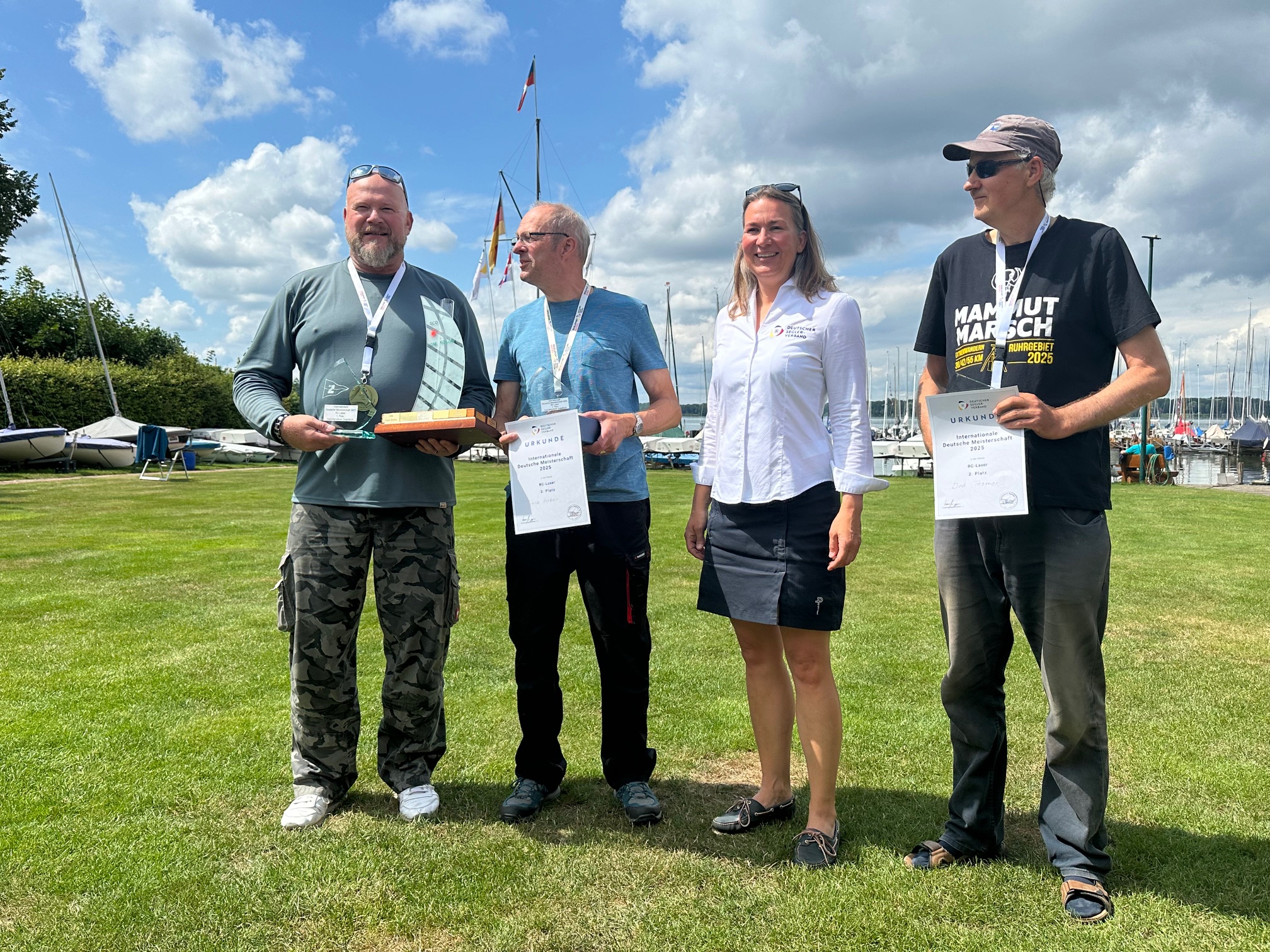 Drei Männer freuen sich bei der Siegerehrung bei einer Segelregatta. Eine Frau gratuliert ihnen.
