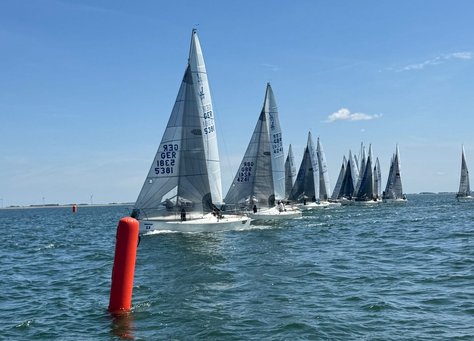 Mehrere Segelboote vom Typ J/24 fahren bei einer Regatta auf eine rote Stabtonne zu