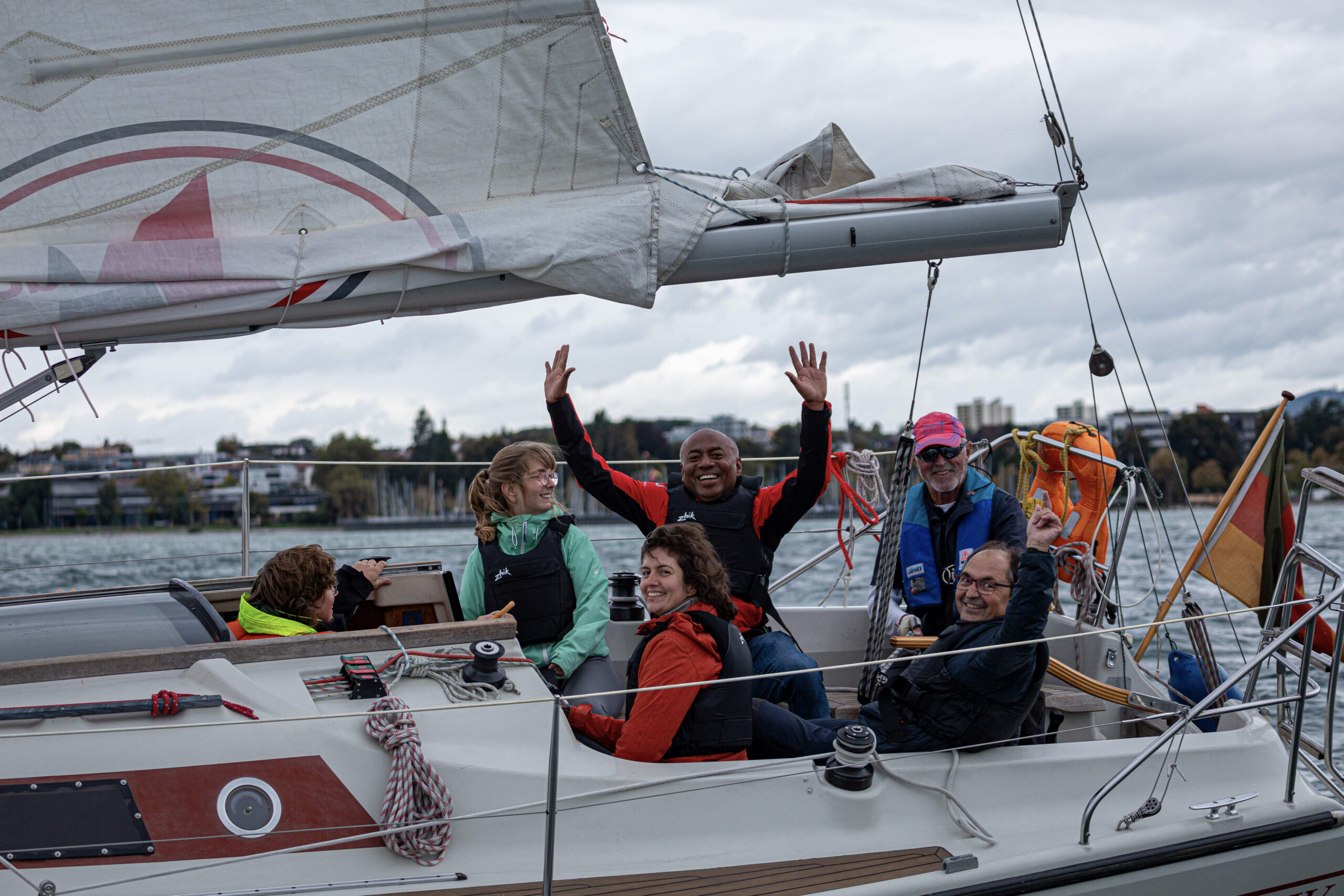 Fröhliche Menschen sitzen auf einer Yacht in der Mitte ein dunkelhäutiger Mann der die Arme hoch hebt