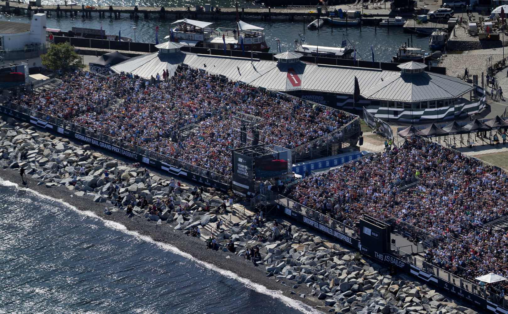 Sehr viele Menschen auf einer Tribüne am Wasser.