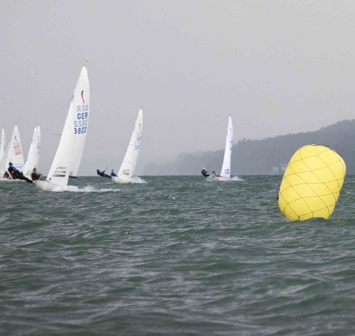Jollen auf einer Regatta bei trübem Wetter, im Vordergrund eine große gelbe Regattatonne.