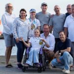 Ein Mädchen im Rollstuhl mit einer Medaille in der Hand umringt von Erwachsenen