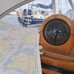 Eine Seekarte mit einem Kompass auf einer Yacht im Hintergrund das Heck einer dunkelblauen Yacht