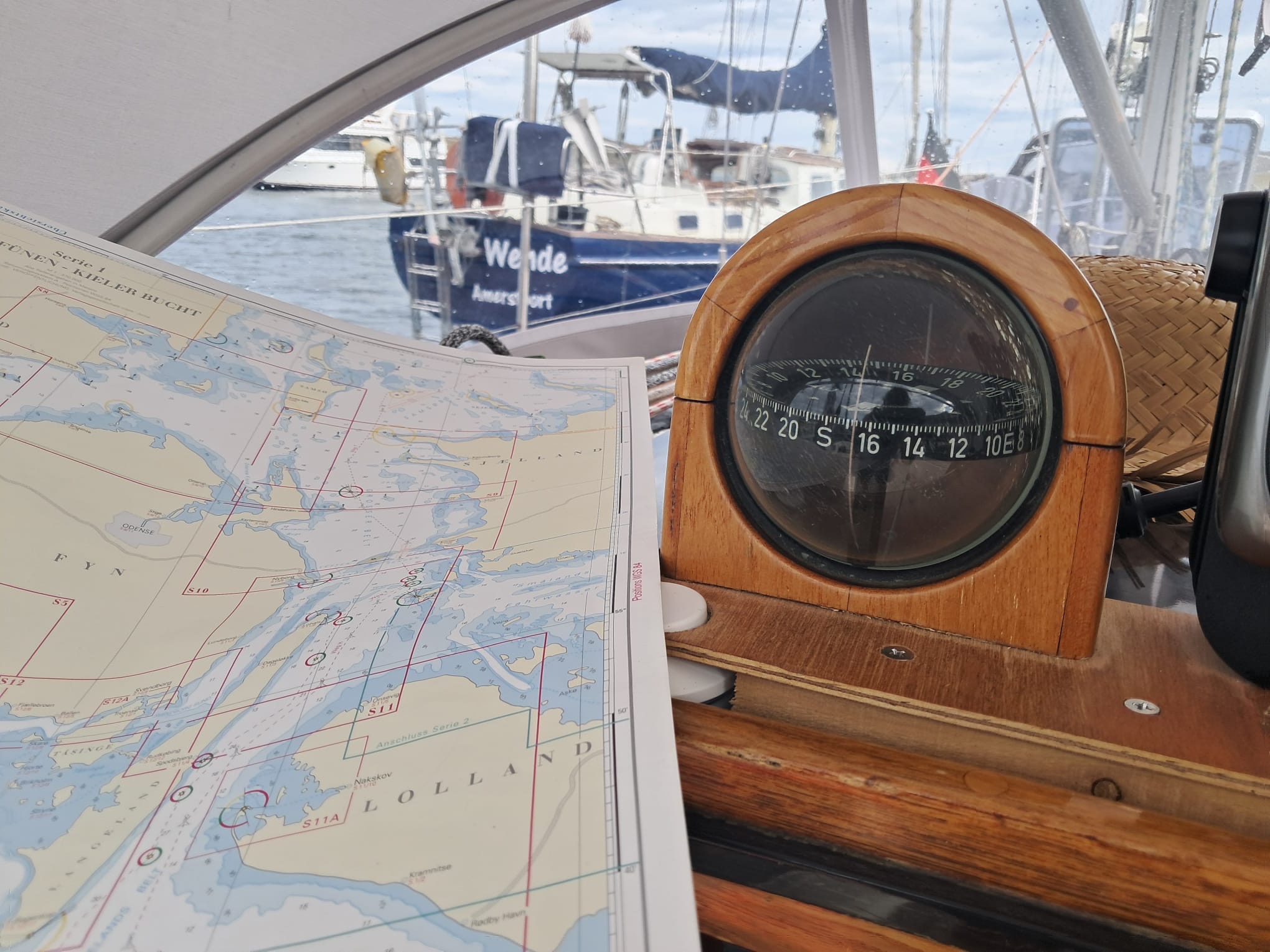 Eine Seekarte mit einem Kompass auf einer Yacht im Hintergrund das Heck einer dunkelblauen Yacht