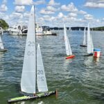 Kleine Modell-Yachten segeln auf dem Wasser, im Hintergrund sind einige Motoryachten zu sehen.