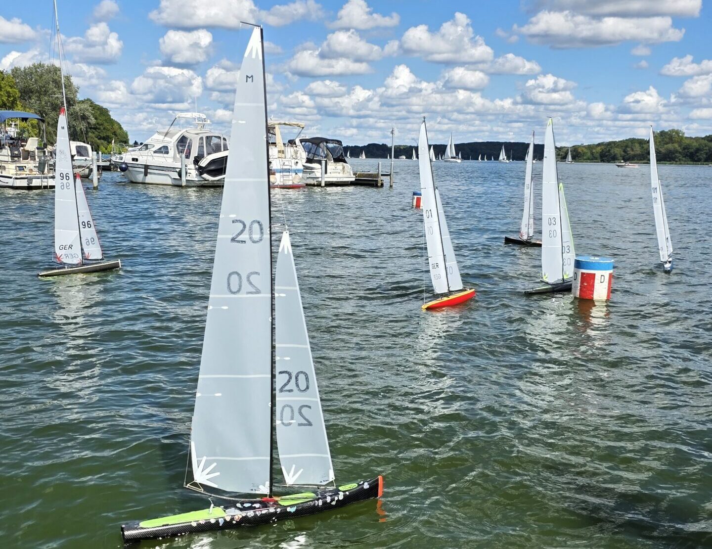 Kleine Modell-Yachten segeln auf dem Wasser, im Hintergrund sind einige Motoryachten zu sehen.