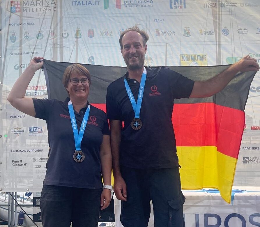 Eine Frau und ein Mann stehen auf einer Bühne mit einer Medaille um den Hals und halten eine Deutschlandflagge hoch.