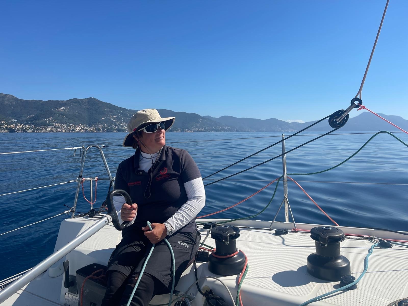 Eine Frau mit Sonnenbrille und Sonnenhut an der Pinne einer Segelyacht im Mittelmeer.