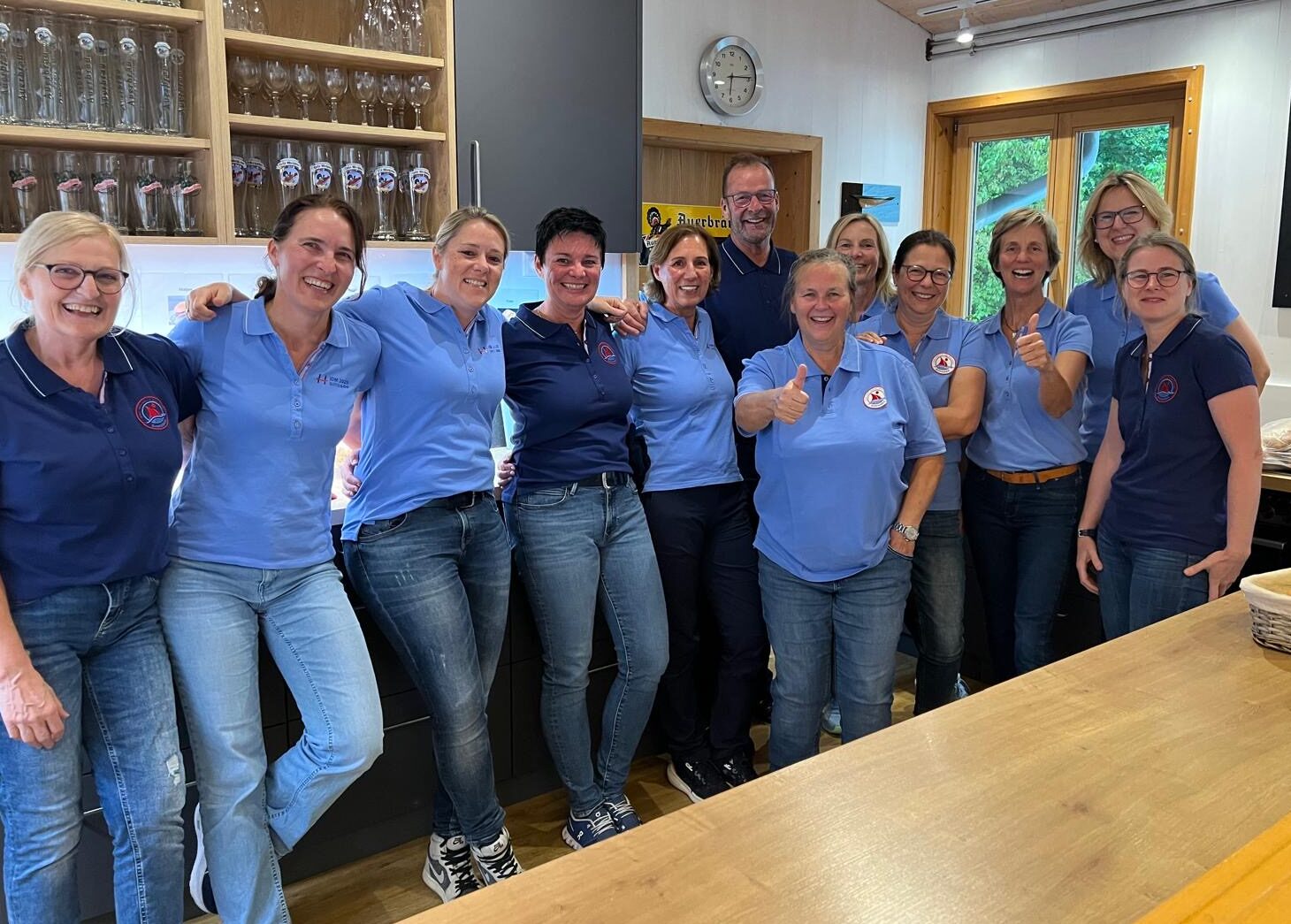 Frauen mit blauen Polohemden lachen in die Kamera und heben den Daumen