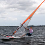Ein Windsurfer surft über das Wasser. Der Himmel ist grau und wolkig