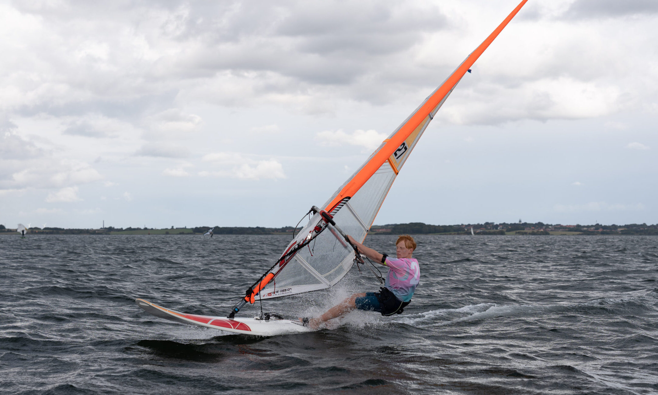 Ein Windsurfer surft über das Wasser. Der Himmel ist grau und wolkig