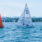 Eine kleine Segelyacht mit der Nummer 1 im Segel vor einer roten Regattamarke auf einem See.