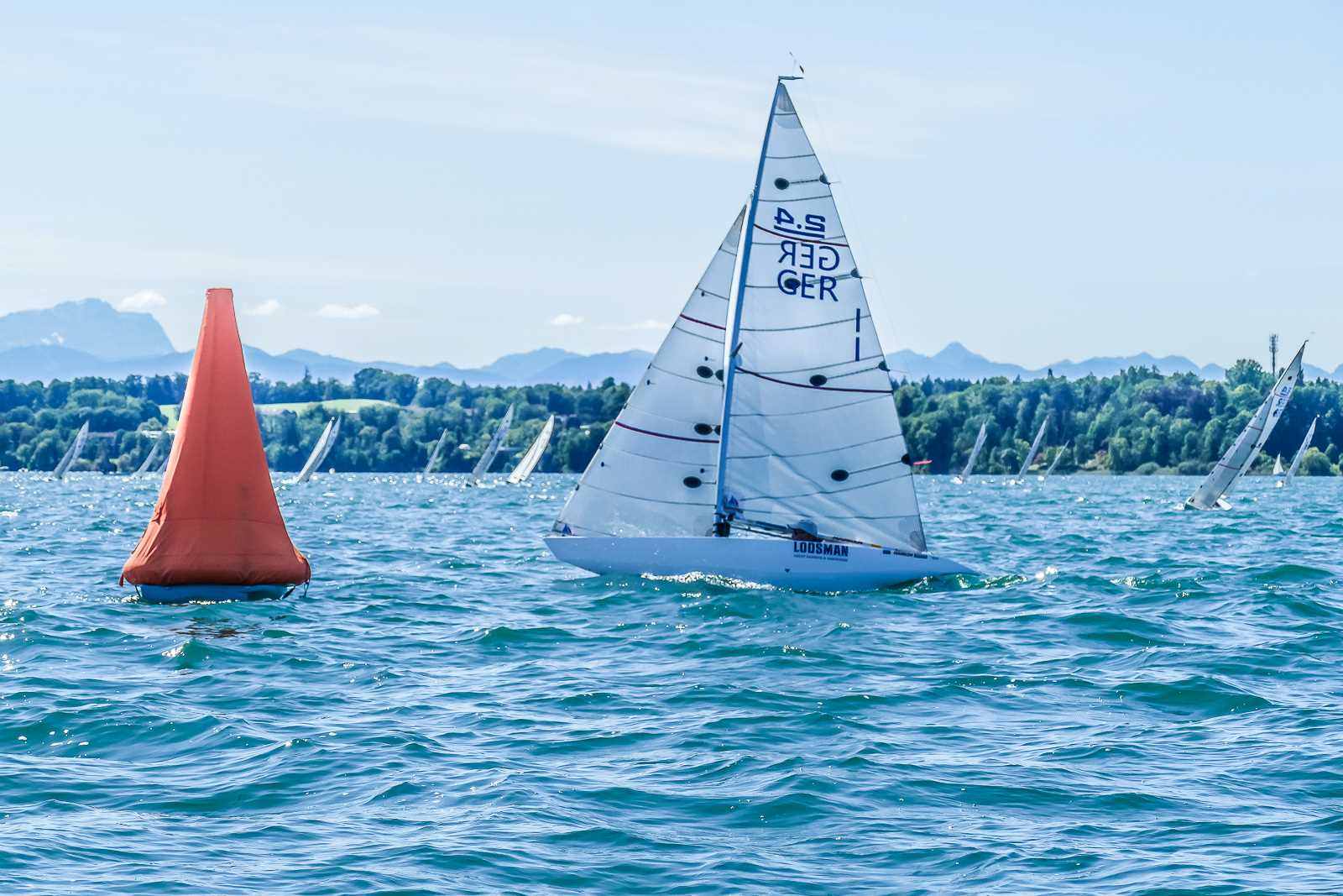 Eine kleine Segelyacht mit der Nummer 1 im Segel vor einer roten Regattamarke auf einem See.