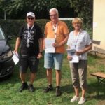 zwei Männer und eine Frau halten Urkunden in der Hand, um ihre Hälse hängen Medaillen. Sie freuen sich.