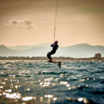 Ein Kitesurfer ist vor Sardinien unterwegs. Er hat ein Foilboard und springt aus dem Wasser.