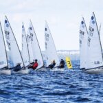 Mehrere Jollen vom Typ Europe, die Boote haben helle Rümpfe und weiße Segel, die Segler sitzen alle auf der Kante der Boote.