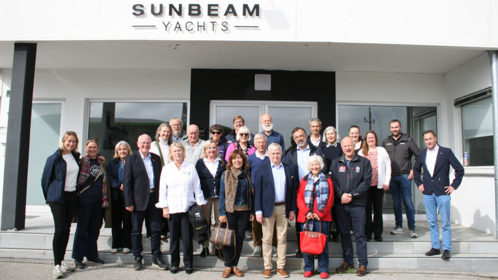 Die Mitglieder der European Boating Association haben sich zum Gruppenbild vor dem Eingang zur österreichischen Werft Sunbeam aufgestellt. Recht mittig steht Mona Küppers in weißer Bluse.