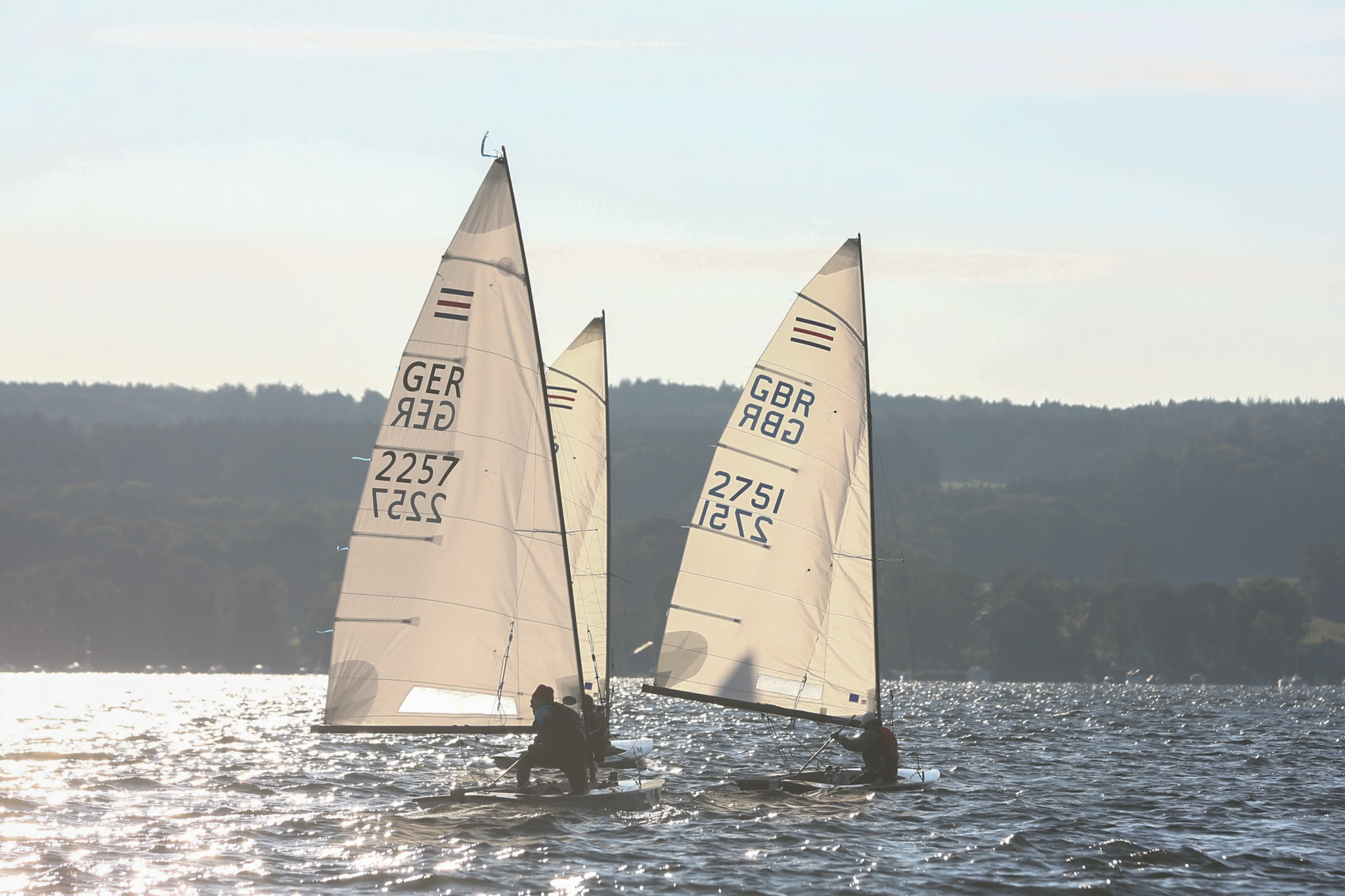 Drei Jollen mit weißen Segeln die vom Sonnenlicht angestrahlt werden.