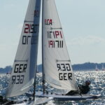 Zwei ILCA Jollen, auch als Laser bekannt, segeln gegen den Wind, ihre Segel überkreuzen sich optisch.
