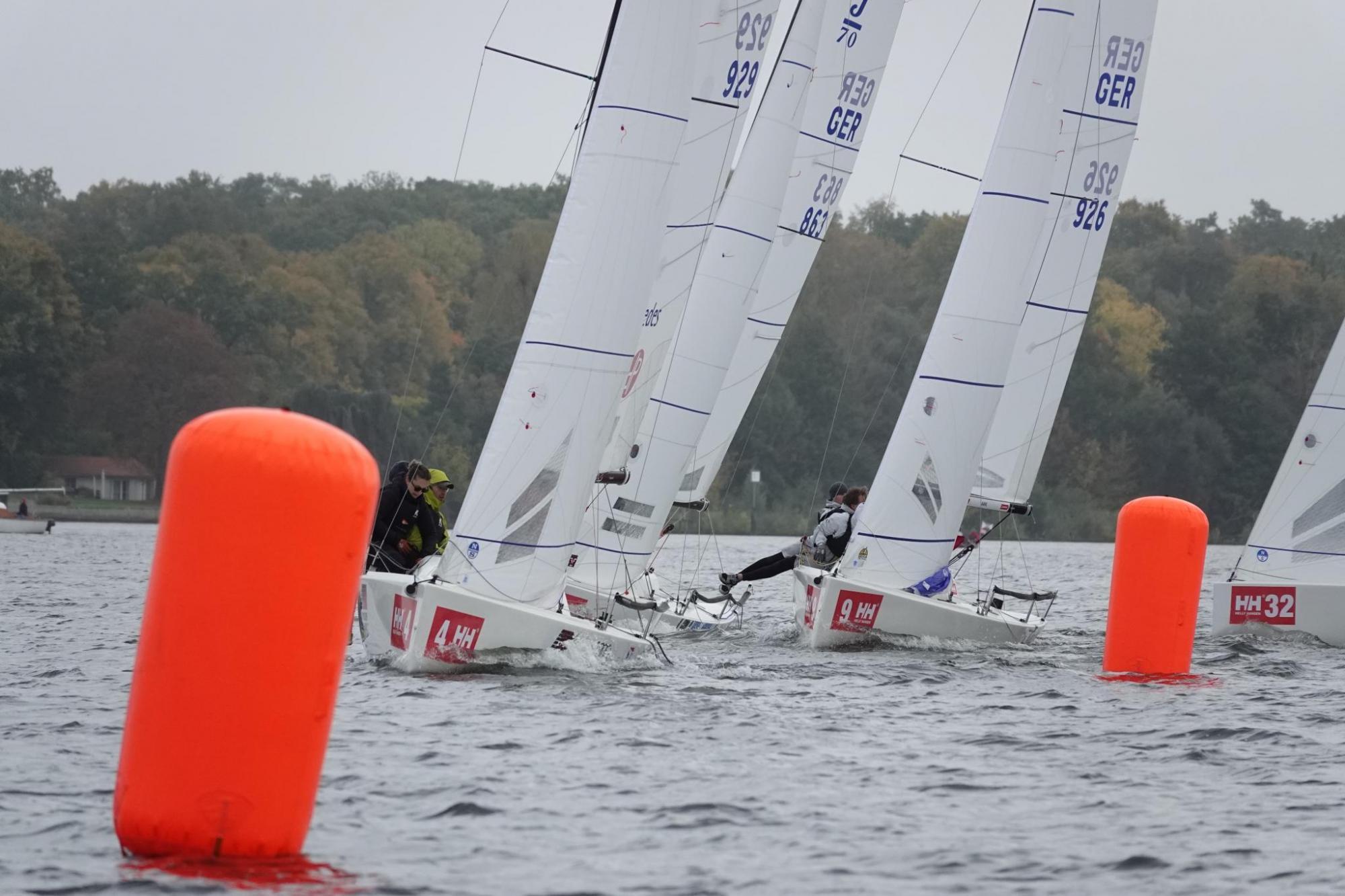Zwei orangefarbene Bahnmarken auf einer Regatta die von mehreren weißen Booten vom Typ J/70 gerundet werden.
